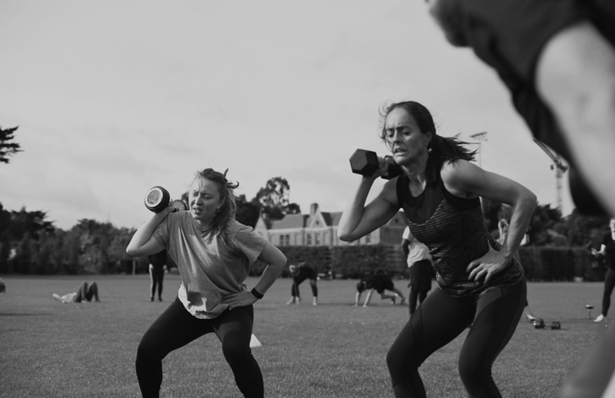 Black and white photograph of two members doing dumbbell squats outdoors on grass