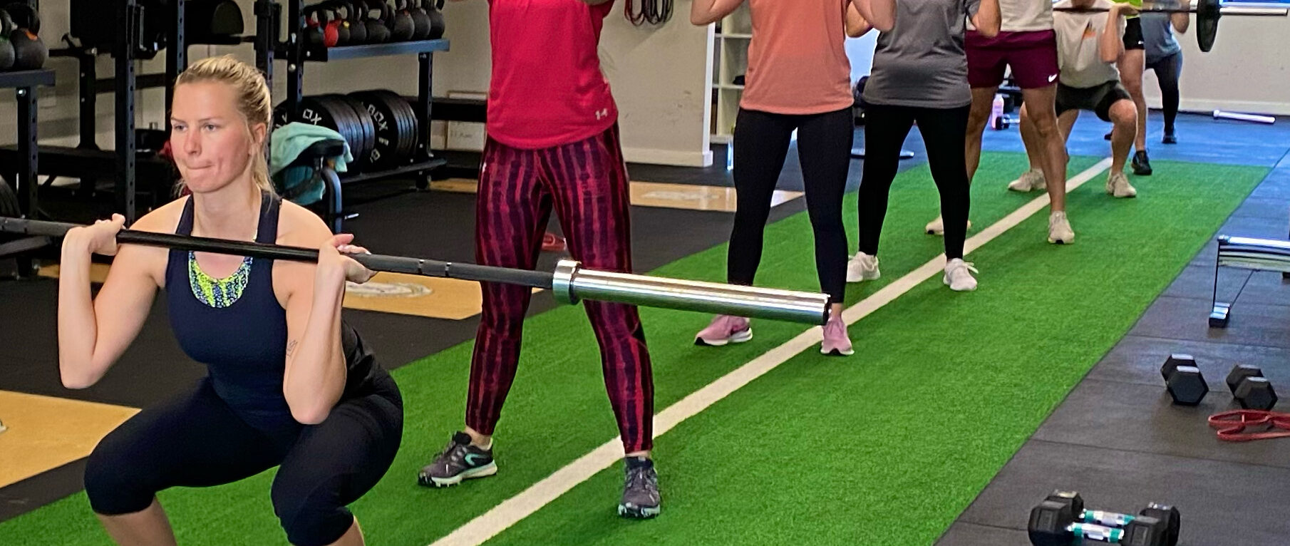 A member front squatting a barbell in the studio with the rest of the class training behind