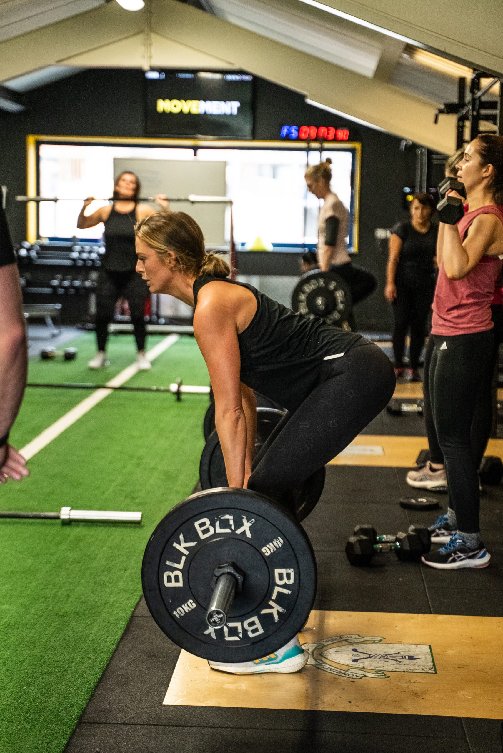 A group class working with dumbbells in the studio under the lit Movement sign